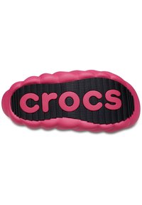 Roze Crocs-zool met een golvende rand, voorzien van een gestructureerd zwart oppervlak en een opvallend roze 'crocs' logo. Lichtgewicht en flexibel materiaal.