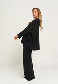 Czarny, oversize sweter i dopasowane szerokie spodnie wykonane z miękkiego materiału, stylizowane z białymi trampkami. Ubranie ma luźny, swobodny krój.