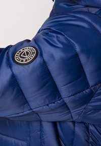 Navy blue puffer jacket featuring quilted sections, smooth texture, and a round logo patch on the left sleeve.