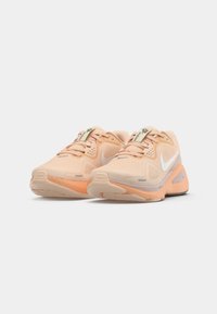 Een paar perzik- en oranje sport sneakers met witte Nike swoosh logo's en veters, naast elkaar geplaatst op een witte achtergrond.