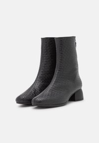 Bottines noires avec une texture tissée, bout pointu et un petit talon carré, présentant une surface lisse et une finition brillante.