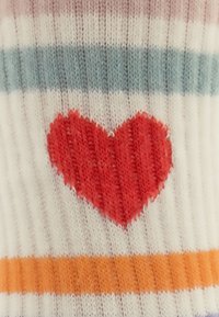 Stricksocken mit weißen, rosa und blauen Streifen, die in der Mitte ein großes rotes Herz aufweisen. Zarte gerippte Textur über die gesamte Socke.