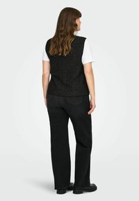 Črna teksturirana jopa brez rokavov, kombinirana z belo majico in črnimi kavbojkami. Obleka ima raven kroj in osnovno kovinsko opremo.