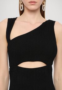 Zwart geribbeld jurkje met een asymmetrisch ontwerp met één schouder en een open uitsnijding bij de taille, waardoor een textuurstof zichtbaar is.