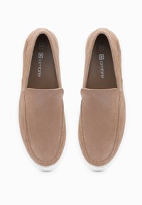 Béžové slip-on boty vyrobené z měkkého semiše, s oválnou špičkou, prošívanými švy a bílou gumovou podešví. Logo je viditelné uvnitř.
