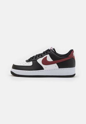Baskets basses avec des panneaux noirs, blancs et bordeaux, lacets noirs, logo Nike bordeaux et semelle blanche avec le mot « Air » embossé.