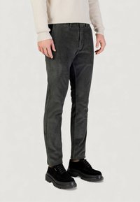 Pantaloni di velluto a coste verde scuro con vestibilità slim e strisce verticali testurizzate, abbinati a scarpe stringate nere con suola robusta.