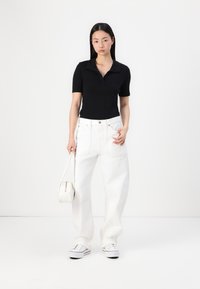 Polo noir, jeans blancs à jambes larges et baskets blanches. Un petit sac à main blanc. Design simple, haut ajusté et couleurs contrastées.