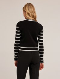 Zwart cropped vest met zwart-witte gestreepte mouwen. Heeft een geribbelde textuur en witte afwerking op de kraag en tailleband.
