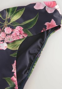 Badkläder med en mörk marinbakgrund, prydd med ett blommönster i rosa och grön. Slät tyg med en kontrasterande stickad kant.