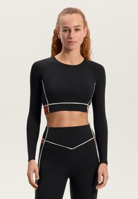 Fekete, hosszú ujjú, haspóló fehér díszítésekkel és barna panellel. Kerek nyakkivágással és testhezálló kialakítással. Fekete, magas derekú leggingsszel párosítva.