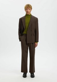 Pruun ülikonnakomplekt, mis koosneb kahekordse nööpimisega bleiserist ja laiade säärtega pükstest, kombineeritud soonikkoes rohelise kõrge kaelusega kampsuniga. Silmapaistev sile tekstuur, minimalistlik disain.