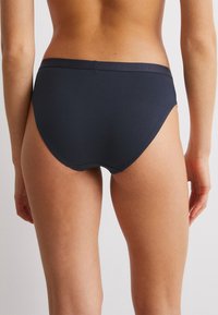 Marinblå högmidjade trosor i mjuk bomullsblandning, med en slät midja som har en subtil präglad logotyp och sömlösa kanter.