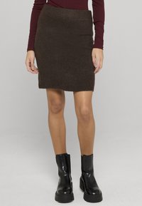 Mini-jupe en maille marron avec une ceinture côtelée, présentant une texture douce et une silhouette ajustée. Associée à des bottines noires épaisses.