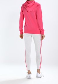 Rosa huvtröja med mjuk textur kombinerad med ljusgrå leggings som har sidostråk i rosa, komplett med vita sneakers.