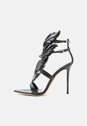 Black high-heeled sandal with wing-shaped glossy decorative elements and double ankle straps with silver buckles.
