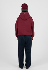 Burgundowa krótka bluza z kapturem, w połączeniu z ciemnonawigacyjnymi spodniami o szerokich nogawkach i bocznymi paskami. Zaprojektowana w luźnym kroju z prążkowanymi mankietami.