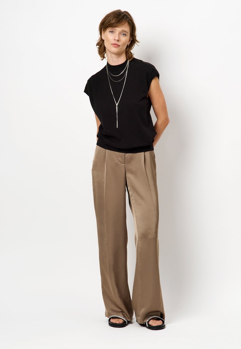 Zwarte kortegalm top, lichtbruine satijnen wijdvallende pantalon, gelaagde zilveren ketting, platte zwarte sandalen. Eenvoudige, schone, moderne look.