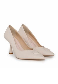 Zapatos de tacón alto de cuero beige con punta afilada y un lazo decorativo en la parte frontal. Los tacones tienen una forma única y esculpida.