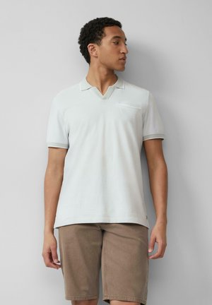 Helles graues Poloshirt mit kurzen Ärmeln und V-Ausschnitt, kontrastierenden Abschlüssen und einer Brusttasche. Kombiniert mit beigen Shorts. Glatte Stoffstruktur.