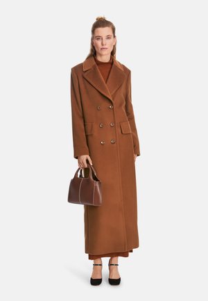 Brown double-breasted coat with large lapels, made of textured fabric. Brown handbag with contrast stitching. Black heels. Long silhouette.