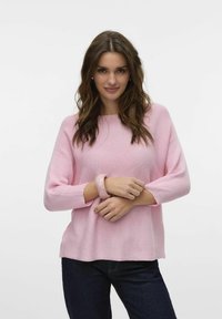 Maglione rosa a maglia con una vestibilità ampia, scollatura rotonda e maniche a tre quarti. Tessuto strutturato con motivo a coste. Jeans scuri e un braccialetto chiaro.