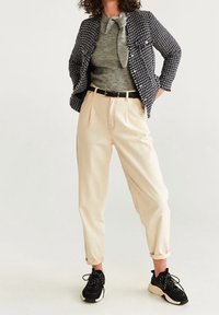 Černobílý texturovaný blazer, světle šedý svetr s mašlí, krémové kalhoty a černé tenisky s bílou podrážkou. Neformální souprava.