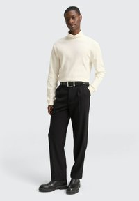 Witte geribde coltrui, zwarte geplooide broek, zwarte riem met metalen gesp, en zwarte chelsea boots. Eenvoudig en elegant design.