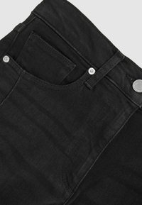 Mustad denim püksid, millel on tavaline vöökoht, esitasku ja metallist kaunistused, esitatud nurga all, koos tekstuuriga kangaga.