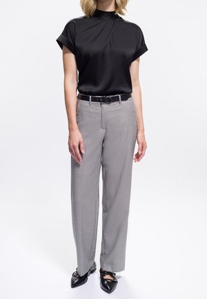 Blusa nera a maniche corte con collo alto, abbinata a pantaloni grigi chiari con texture e décolleté neri a punta con dettagli decorativi.