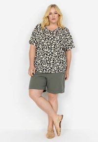Svart och gräddfärgad mönstrad t-shirt med kort ärm, olivgröna shorts och beige vävda sandaler. Avslappnad passform med V-ringning.