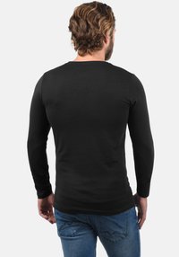 Schwarzes Langarmshirt aus weichem Stoff, figurbetontes Design, glatte Textur. Kombiniert mit blauen Jeans, Ansicht von hinten.