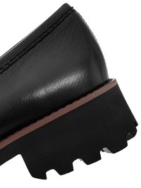 Gros plan sur le talon d'une chaussure en cuir noir avec une semelle en caoutchouc épaisse et robuste et un détail de couture marron.