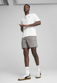 Hvid kortærmet t-shirt med sort Puma-logo, grå cargo shorts, hvide og grå sneakers med sorte accenter og hvide ribbede sokker.
