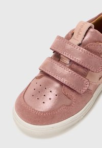 Sneaker rosa con una combinazione di texture lucide e scamosciate, due cinturini in Velcro, design con punta perforata e suola in gomma bianca.