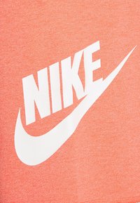 Logotipo blanco de Nike con el símbolo Swoosh sobre un fondo de tela texturizada naranja.