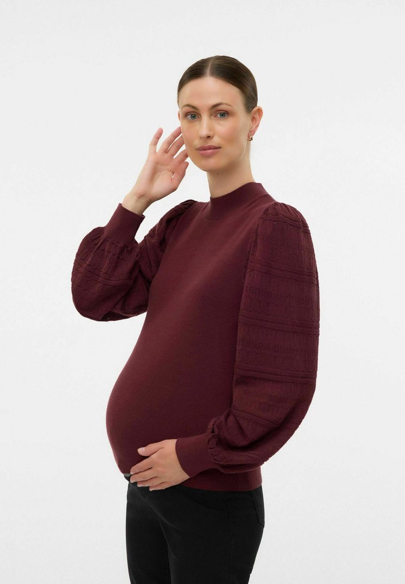 Bordeaux sweatshirt med texturerade puffärmar, ribbat halsband och muddar, samt en avslappnad passform. Bärs över en synlig mage, tillsammans med svarta byxor.