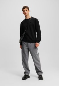 Felpa nera con polsini a coste, abbinata a jeans larghi grigio chiaro con testo chiaro di lato e sneaker nere.
