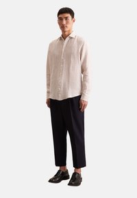 Camicia a maniche lunghe a righe beige e crema con colletto, abbinata a pantaloni sartoriali scuri e scarpe eleganti nere.
