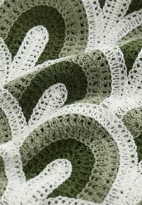 Gros plan d’un tissu au crochet texturé avec des motifs circulaires en fil vert foncé, vert clair et blanc.