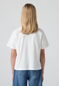 Camiseta blanca de manga corta con un corte holgado, hecha de algodón, con un cuello redondo y una textura suave. Combinada con jeans de cintura alta azules.