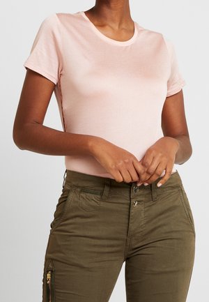 Lyserød T-shirt med korte ærmer og rund halsudskæring, kombineret med olivengrønne bukser med lynlåsdetaljer og en tætsiddende pasform.