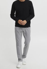 Jersey negro de punto con cuello redondo, pantalones grises claros de corte entallado con rayas sutiles, combinados con zapatillas blancas. Diseño sencillo y silueta ajustada.