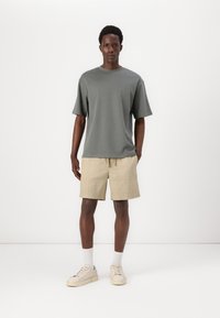 Graues T-Shirt mit kurzen Ärmeln, beiger Shorts mit Kordelzug, weiße Crew-Socken und helle Sneaker. Einfaches Design mit lockerer Passform und weichem Material.