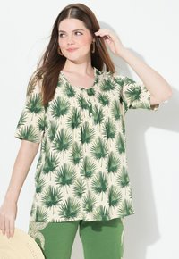 Top de manga corta en beige con estampado de hojas de palma verdes, con escote redondo, pliegues y detalles de botones. Combinado con pantalones verde oscuro.