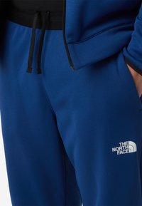 Niebieskie dresy z miękkiej tkaniny, czarną talią z troczkami oraz białym logo na dolnej części nogawki.