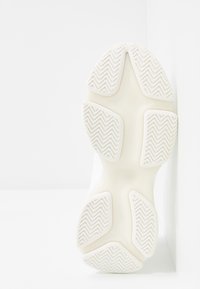 Kenkien pohja, jossa on teksturoitu valkoinen kumipinta, herringbone-kuvioita ja pyöristettyjä muotoja pidon ja vakauden takaamiseksi.