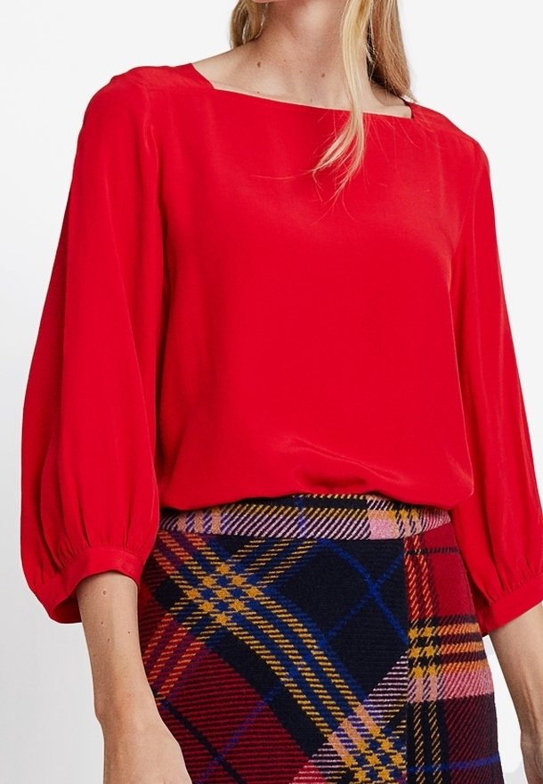 Rode zijden blouse met een vierkante halslijn en pofmouwen, gecombineerd met een gestreepte wollen rok in blauw, rood en gele tinten.