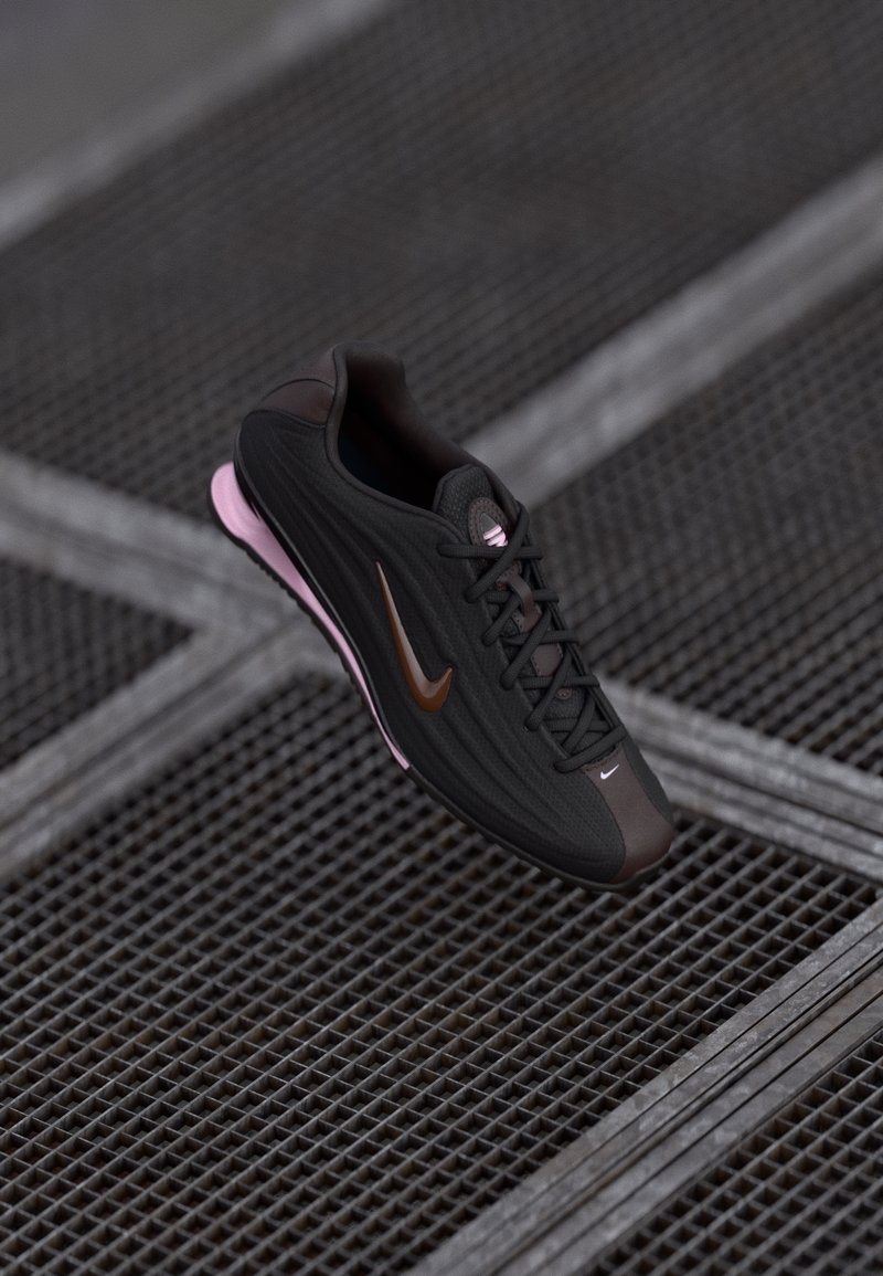Crne i smeđe Nike tenisice s ružičastom potplatom lebde iznad metalne rešetkaste podloge s preklapajućim dijagonalnim linijama.