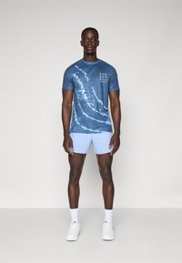 Blå tie-dye trenings t-skjorte med korte ermer og teksten "RUN", parret med lyseblå kortbukser. Materialet ser lett og pustende ut.